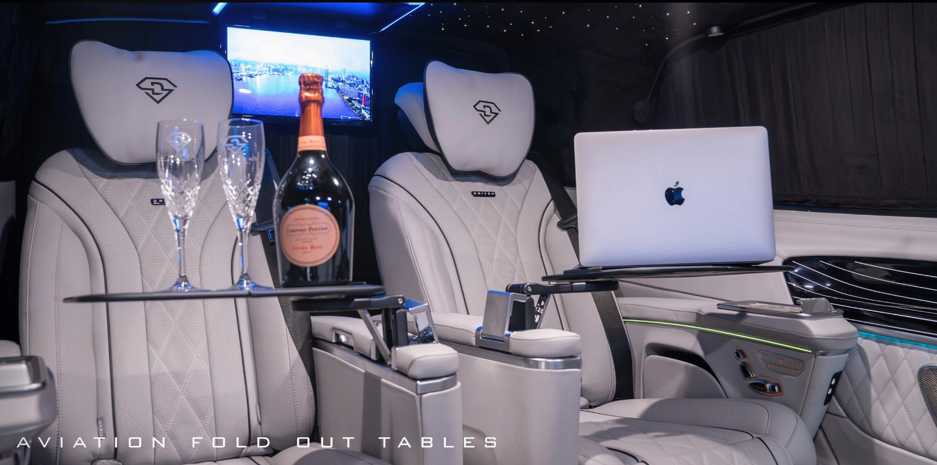 Aviation-style fold-out tables with champagne, glassware and a laptop set up in the cabin